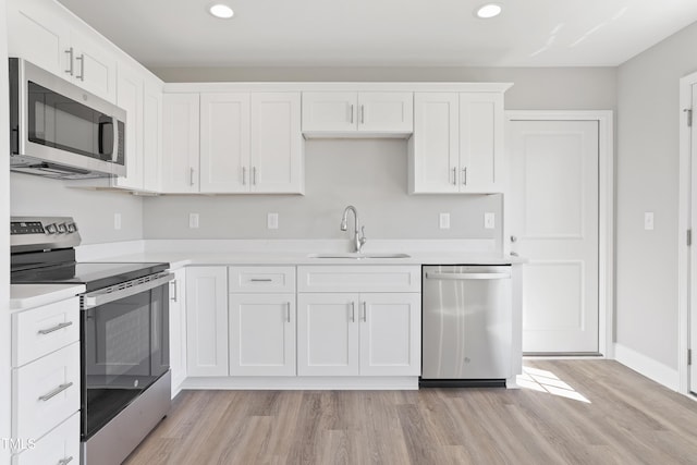 kitchen featuring light wood finished floors, a sink, appliances with stainless steel finishes, white cabinets, and light countertops