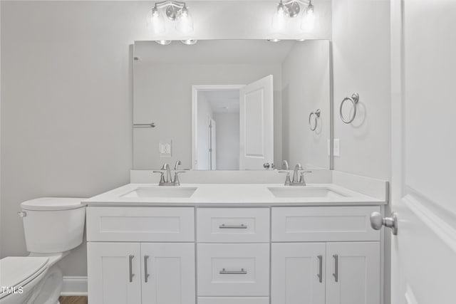 bathroom with double vanity, toilet, baseboards, and a sink