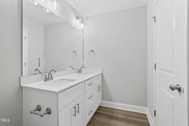 full bath with double vanity, wood finished floors, baseboards, and a sink