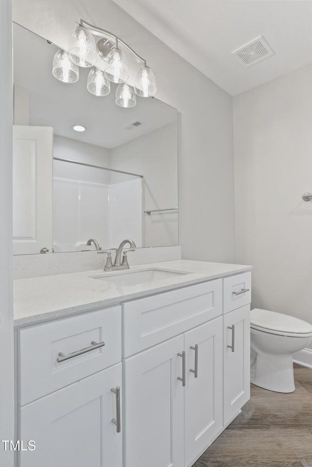 bathroom with vanity, wood finished floors, visible vents, walk in shower, and toilet