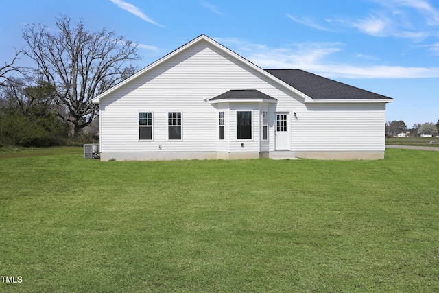 rear view of property featuring a lawn, central AC unit, and roof with shingles