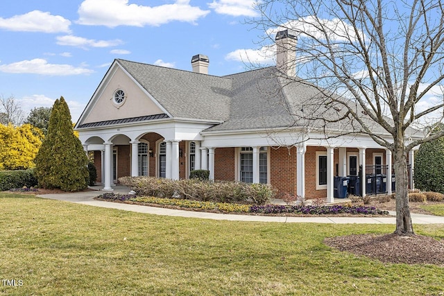 view of front facade featuring brick siding, a standing seam roof, a front yard, and a shingled roof