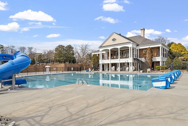 community pool featuring a water slide, stairway, a patio area, and fence