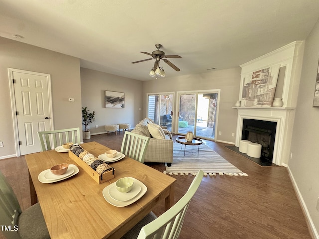 dining room with a fireplace with flush hearth, a ceiling fan, baseboards, and wood finished floors