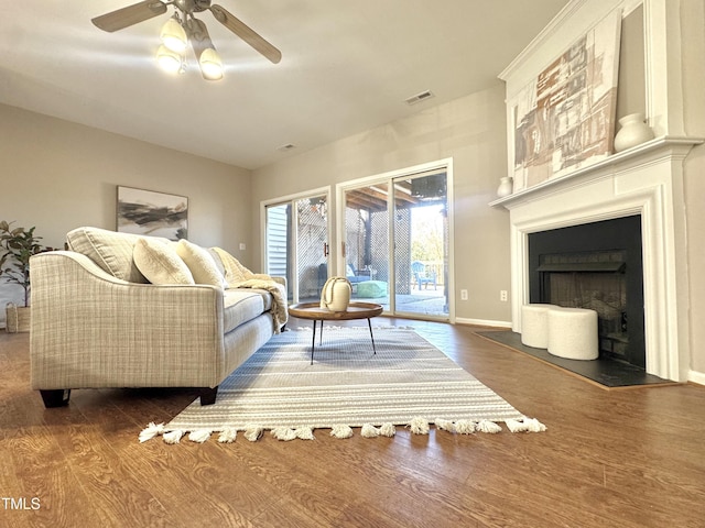 living area with baseboards, visible vents, a ceiling fan, wood finished floors, and a fireplace