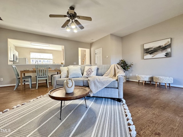 living room featuring dark wood-type flooring, a ceiling fan, and baseboards