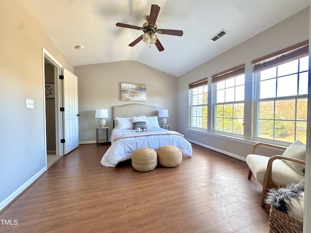 bedroom featuring ceiling fan, wood finished floors, visible vents, baseboards, and vaulted ceiling