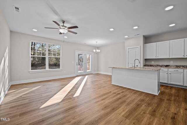 kitchen with white cabinetry, a kitchen island with sink, light stone countertops, decorative light fixtures, and light wood-type flooring