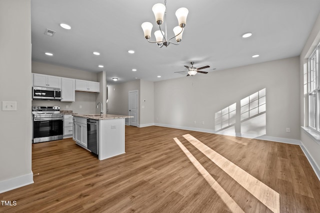 kitchen featuring appliances with stainless steel finishes, sink, white cabinets, hanging light fixtures, and a kitchen island with sink