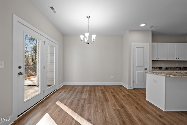 unfurnished dining area with an inviting chandelier and light hardwood / wood-style floors