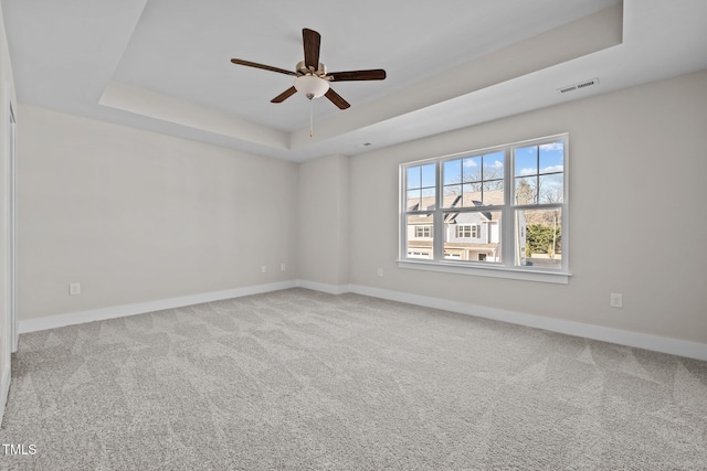 spare room featuring light carpet, a tray ceiling, and ceiling fan