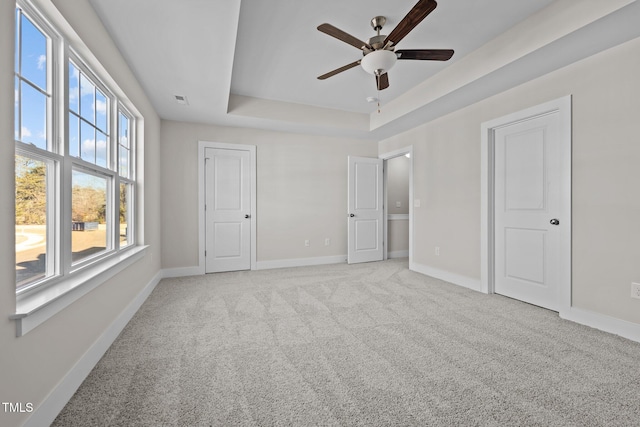 unfurnished bedroom with light carpet, a raised ceiling, and ceiling fan