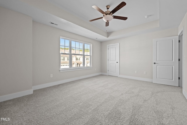 spare room featuring light carpet, a tray ceiling, and ceiling fan