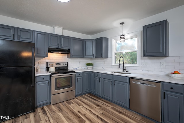 kitchen featuring sink, tasteful backsplash, pendant lighting, appliances with stainless steel finishes, and hardwood / wood-style flooring