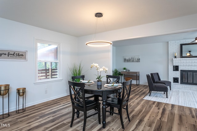 dining space featuring ceiling fan, dark hardwood / wood-style floors, and a brick fireplace