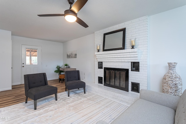 living room featuring ceiling fan, light hardwood / wood-style floors, and a brick fireplace