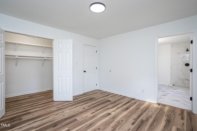 unfurnished bedroom featuring hardwood / wood-style floors, ensuite bathroom, and a closet