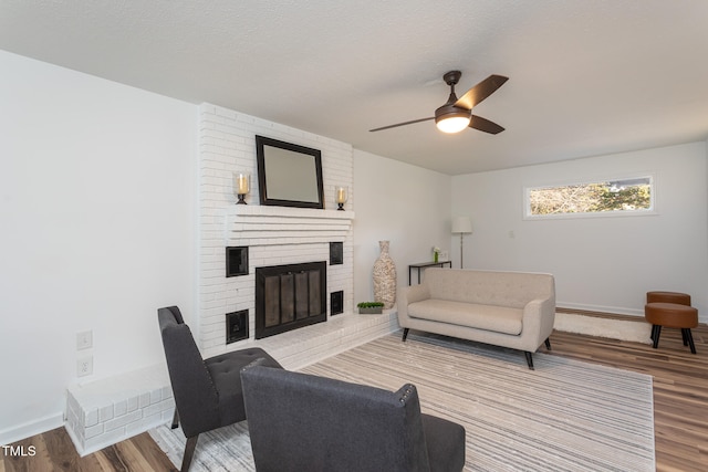 living room featuring ceiling fan, a fireplace, a textured ceiling, and light wood-type flooring