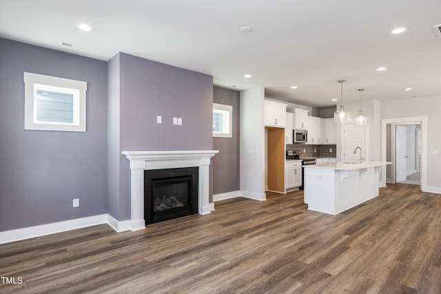 kitchen featuring decorative backsplash, a kitchen island with sink, pendant lighting, white cabinets, and a breakfast bar area