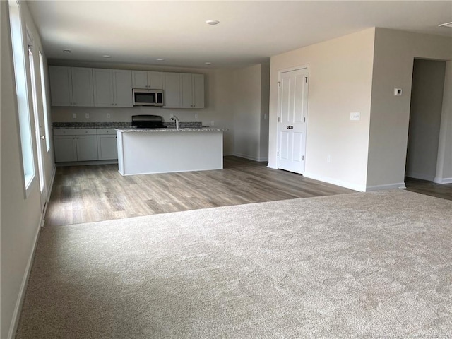 kitchen with an island with sink, carpet flooring, gray cabinetry, stove, and light stone counters