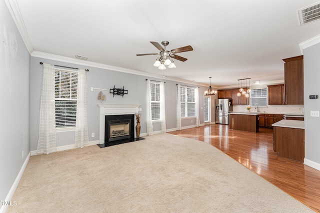 unfurnished living room with ceiling fan with notable chandelier, light colored carpet, sink, and crown molding