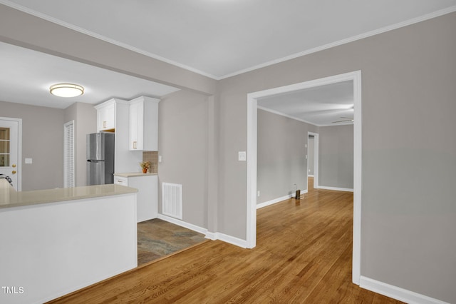 kitchen with hardwood / wood-style floors, white cabinets, crown molding, ceiling fan, and stainless steel refrigerator