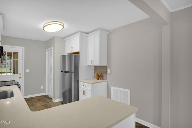 kitchen featuring decorative backsplash, white cabinetry, kitchen peninsula, and stainless steel refrigerator