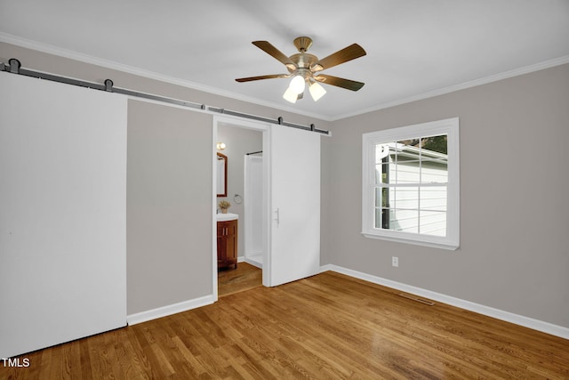 unfurnished bedroom featuring a barn door, hardwood / wood-style flooring, ceiling fan, and ensuite bathroom