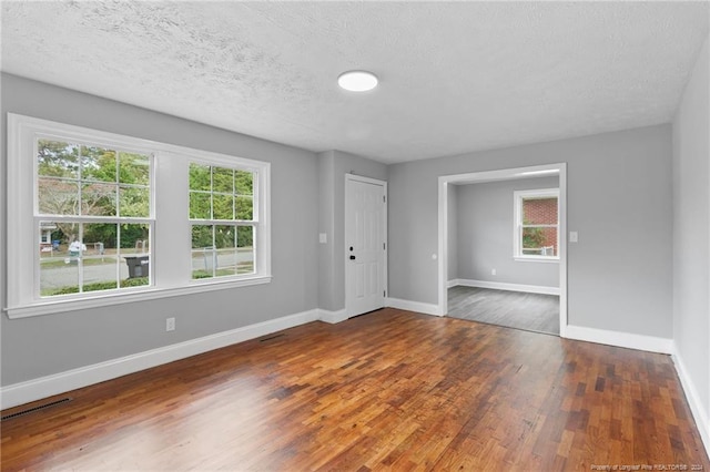 spare room with dark wood-type flooring, a healthy amount of sunlight, and a textured ceiling