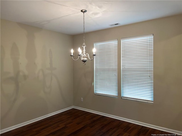 empty room with dark wood-type flooring and a chandelier