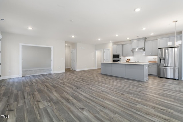 kitchen with appliances with stainless steel finishes, a center island with sink, decorative light fixtures, and light hardwood / wood-style floors