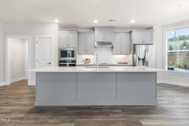 kitchen with dark wood-type flooring, a center island with sink, and stainless steel appliances