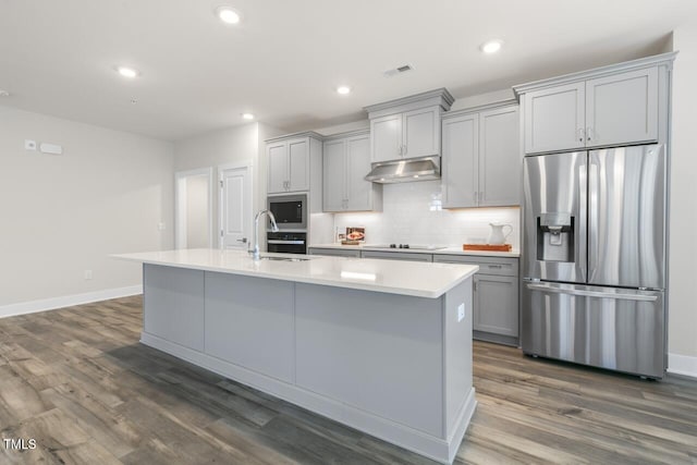 kitchen featuring sink, dark wood-type flooring, stainless steel appliances, gray cabinets, and a center island with sink