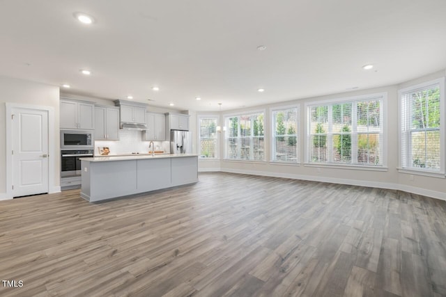 kitchen featuring backsplash, hanging light fixtures, light wood-type flooring, an island with sink, and stainless steel appliances