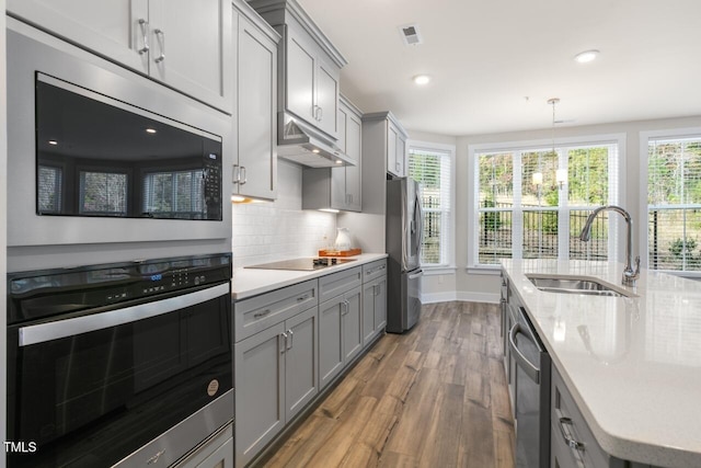 kitchen with gray cabinetry, stainless steel appliances, sink, pendant lighting, and hardwood / wood-style flooring