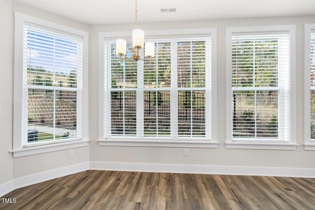 unfurnished dining area with hardwood / wood-style flooring, an inviting chandelier, and a healthy amount of sunlight