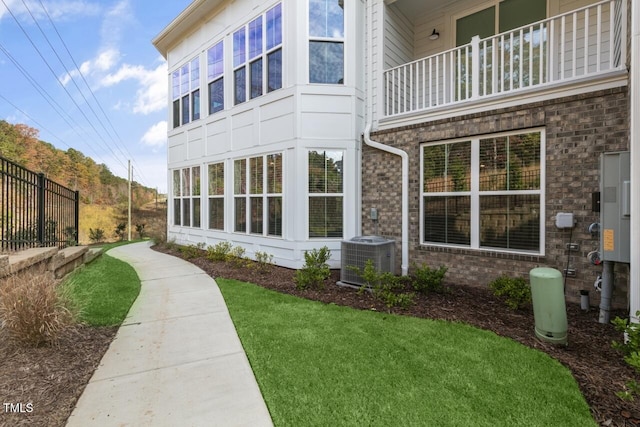 view of home's exterior featuring a balcony, central AC, and a lawn