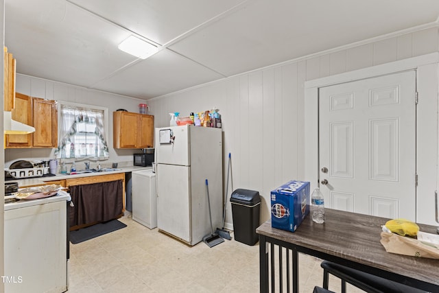 kitchen with wood walls, white appliances, sink, ornamental molding, and washer / dryer