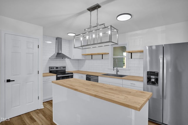 kitchen featuring sink, wall chimney range hood, butcher block countertops, white cabinets, and appliances with stainless steel finishes