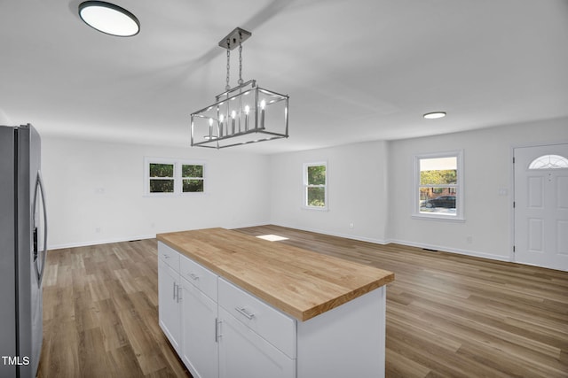 kitchen with butcher block counters, white cabinetry, light hardwood / wood-style flooring, stainless steel fridge, and pendant lighting