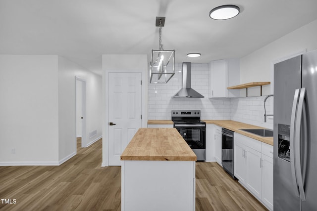 kitchen with appliances with stainless steel finishes, wall chimney range hood, a center island, hanging light fixtures, and butcher block counters