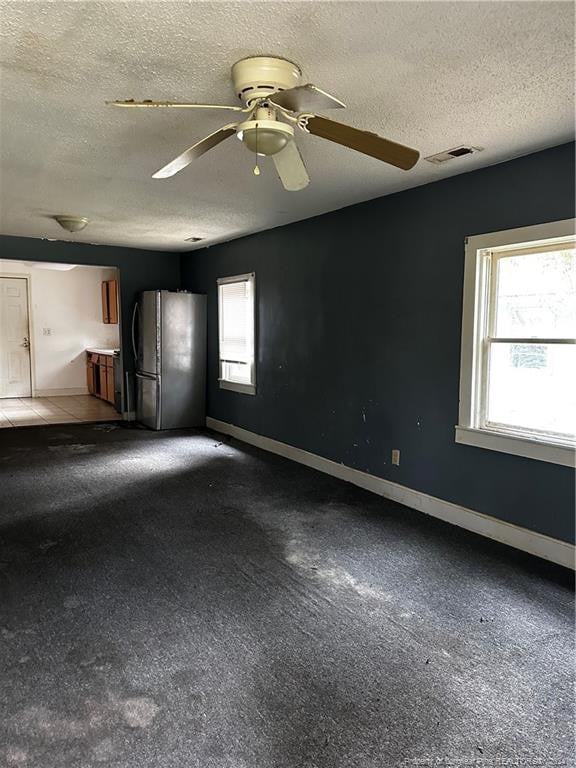 carpeted empty room featuring a textured ceiling, plenty of natural light, and ceiling fan