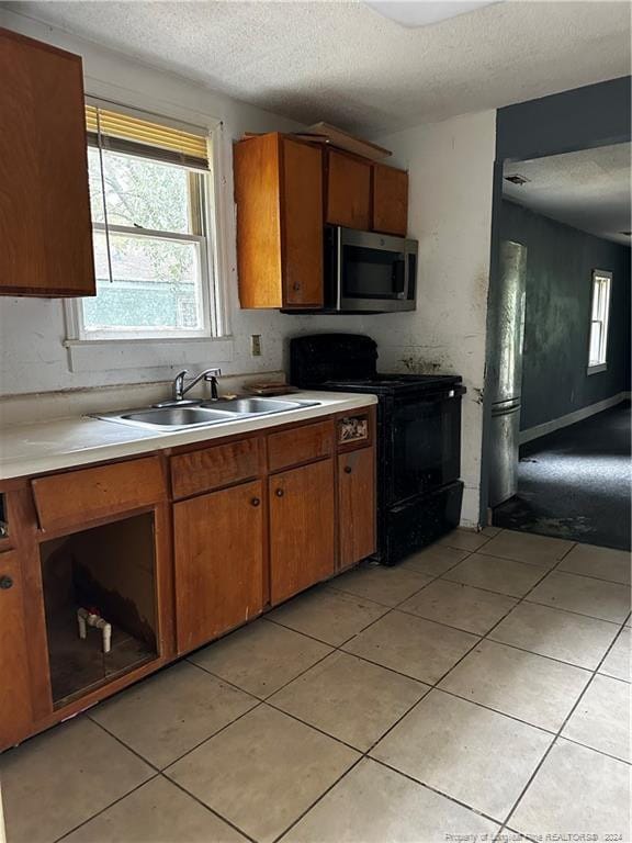 kitchen featuring light tile patterned flooring, a textured ceiling, black range with electric stovetop, and sink