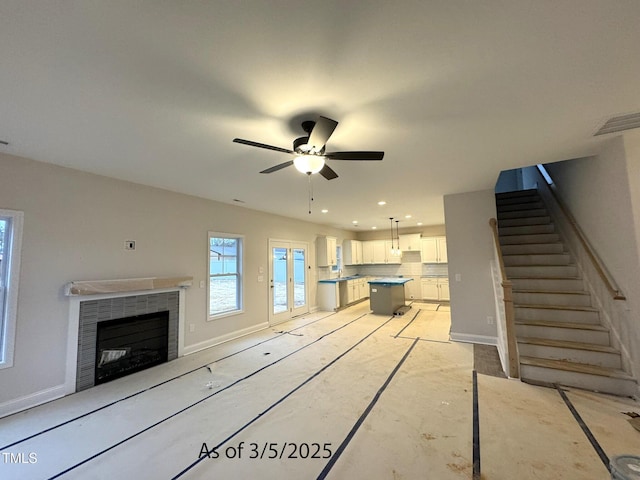 unfurnished living room with a tile fireplace, visible vents, stairway, and baseboards