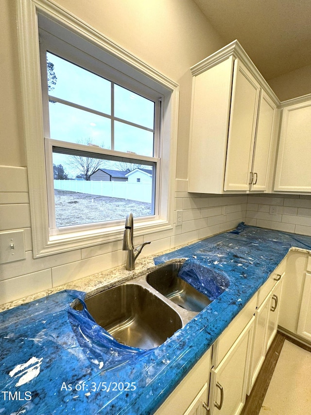 kitchen featuring dark stone counters, white cabinetry, a sink, and backsplash