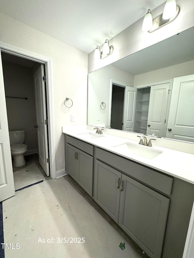 bathroom with double vanity, a sink, toilet, and baseboards