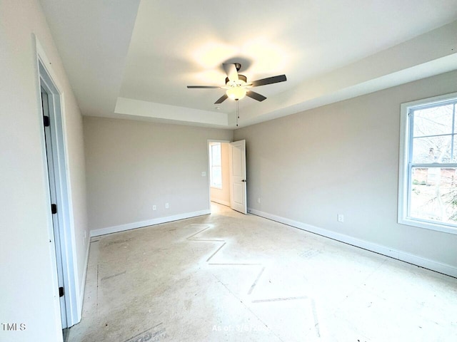 interior space featuring a tray ceiling, a ceiling fan, and baseboards