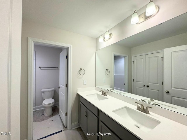 bathroom featuring double vanity, baseboards, toilet, and a sink