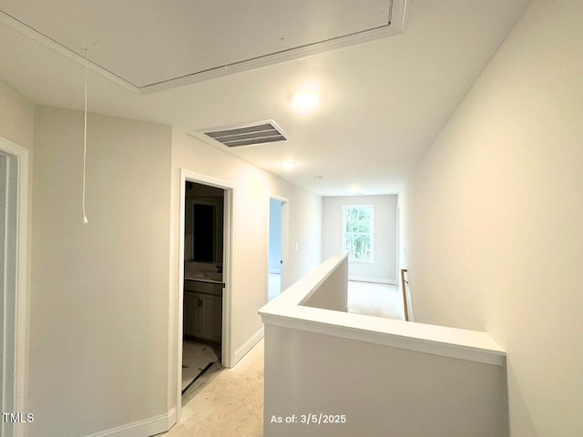 hallway with attic access, baseboards, visible vents, and an upstairs landing