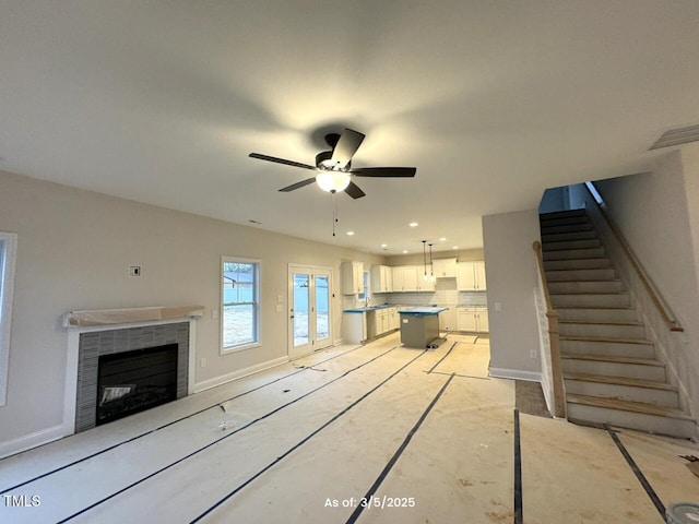 unfurnished living room with stairs, a ceiling fan, visible vents, and baseboards